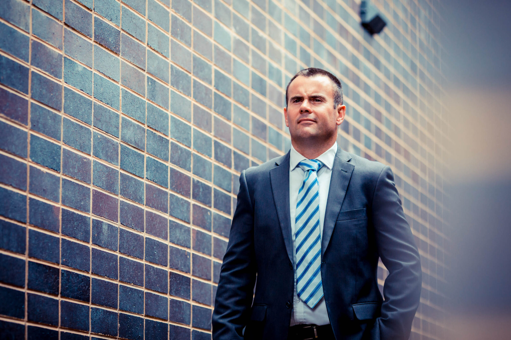 Angus Macleod in a suit against a brick wall